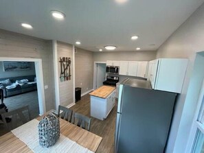 A modern kitchen with white cabinets, a stainless steel refrigerator, and a wooden dining table.