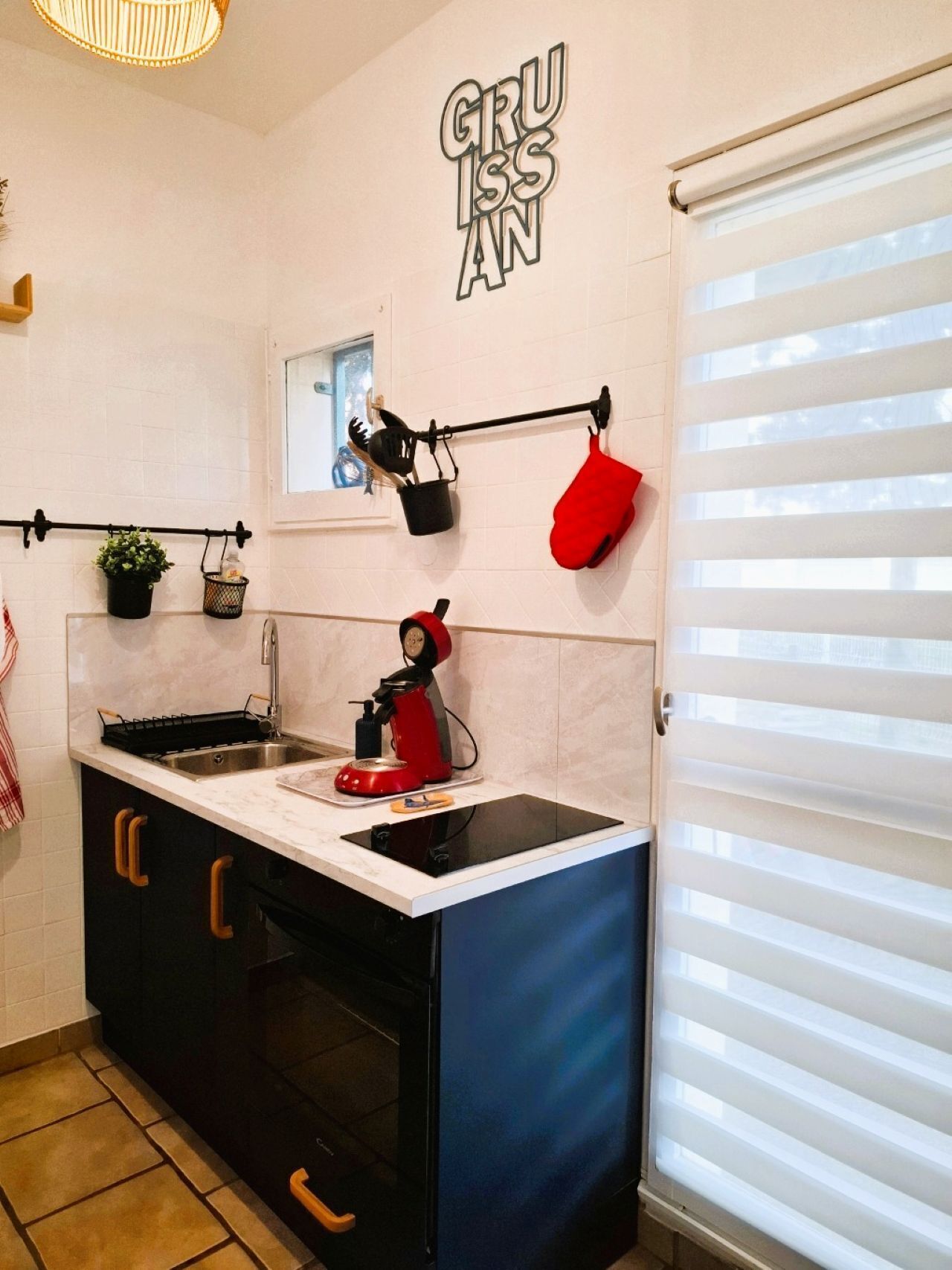 A kitchen with a built-in stove, a sink, and a window with blinds.