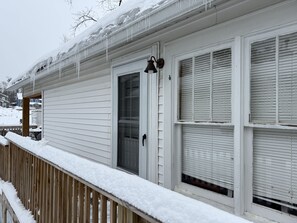 Une maison à l’extérieur blanc, avec une terrasse en bois et un environnement enneigé.