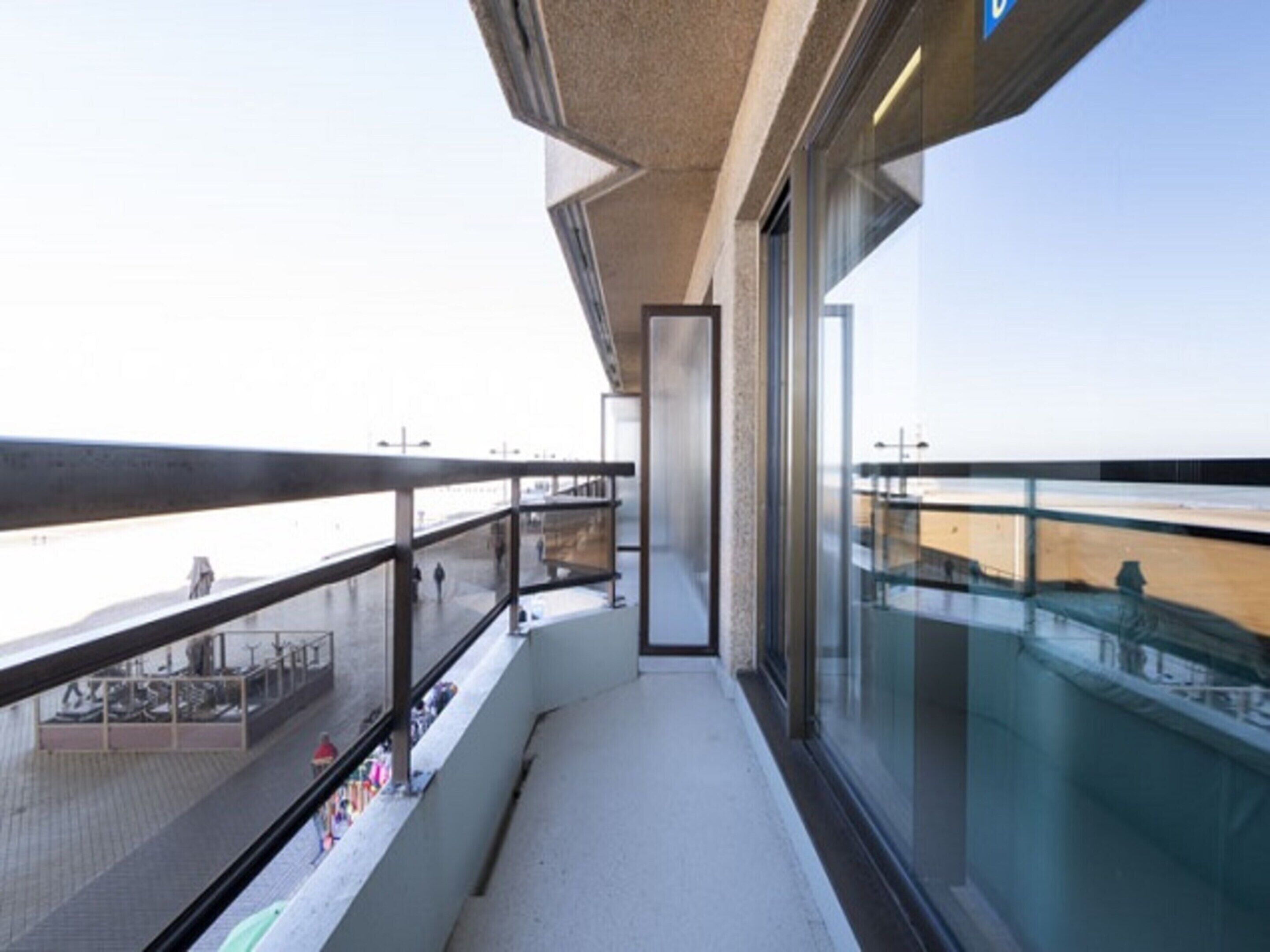 A modern building with a glass facade and a balcony overlooking a beach.