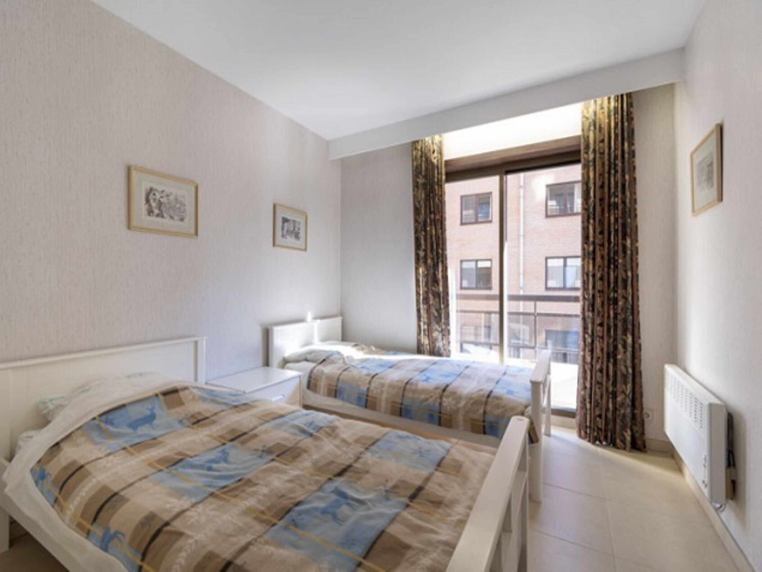 A bedroom with two beds, a window with curtains, and a radiator.