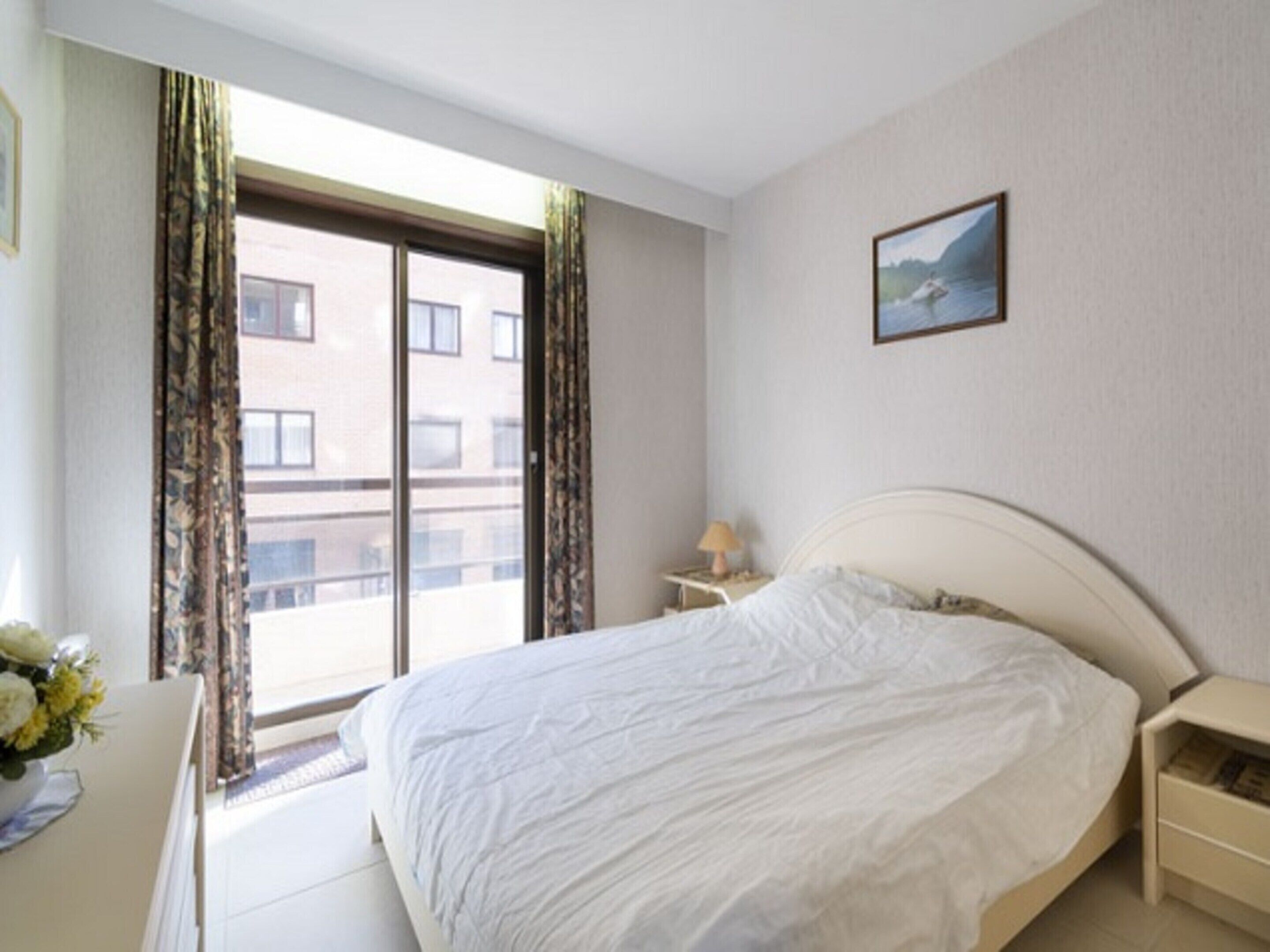 Ett hotellrum med en stor säng, ett nattduksbord, en lampa och ett fönster med gardiner.
