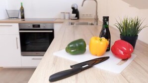 A kitchen with a cutting board, a knife, and three bell peppers. - Vacation apartment *Am Bronnwiesle* (Deggingen)