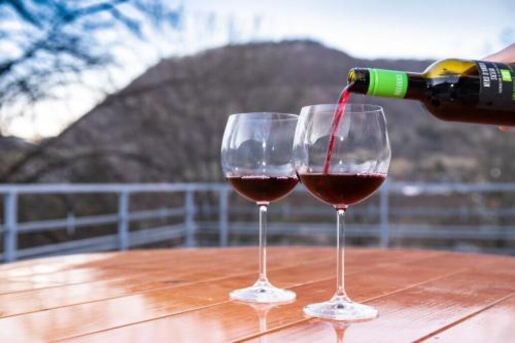 Two wine glasses on a wooden table with a bottle of red wine being poured into one.