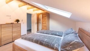 A bedroom with a sloped ceiling, a bed with grey bedding, a wooden wardrobe, and a small plant on the dresser. - Vacation apartment *Am Bronnwiesle* (Deggingen)