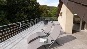 A rooftop terrace with a seating area, a view of the surrounding forest, and a building entrance. - Vacation apartment *Am Bronnwiesle* (Deggingen)