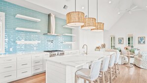 A modern kitchen with white cabinetry, a blue backsplash, and a central island with bar stools.