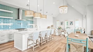 A modern kitchen with white cabinetry, a central island with bar stools, and a dining area with a wooden table and chairs.