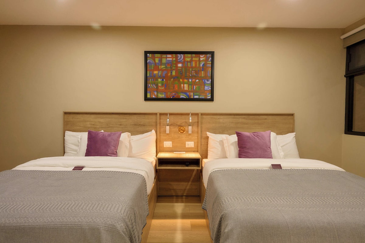A hotel room with two beds, a wooden headboard, a nightstand, and a wall-mounted artwork.