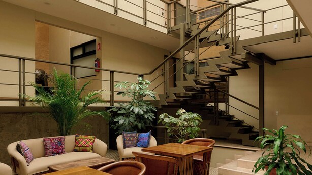 A spacious atrium with a high ceiling, a staircase, and a seating area with tables and chairs. - Suites el Consuelo (Oaxaca)