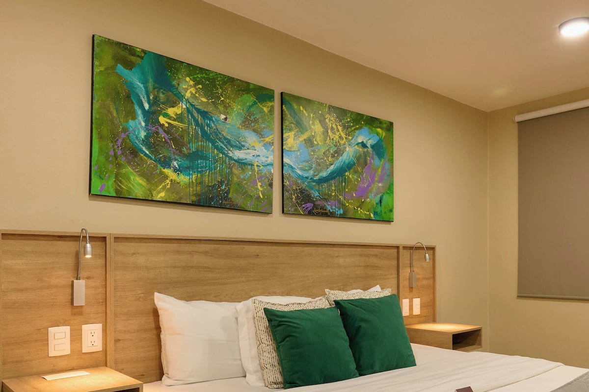 A modern hotel room with a large bed, wooden headboard, two nightstands, and abstract wall art.