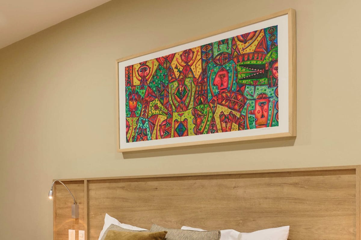 A hotel room with a wooden headboard, a large bed with white bedding, two bedside tables, and a colorful abstract painting on the wall.