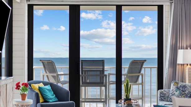 Uma varanda com vista para o mar, duas cadeiras, um sofá e uma pequena mesa com uma planta.