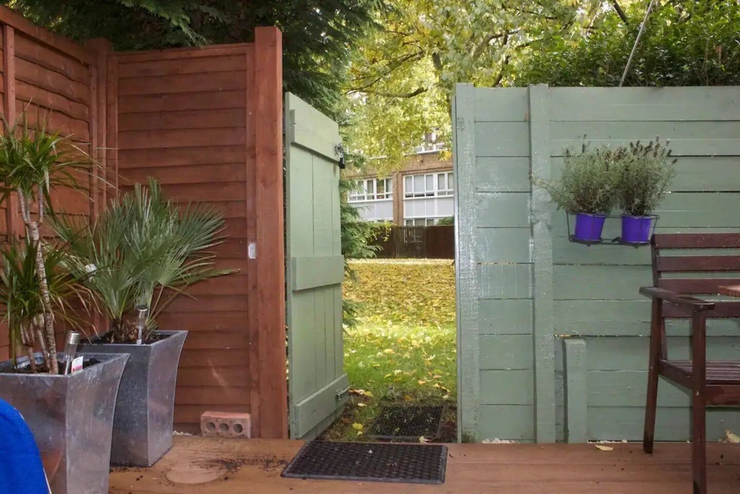 A wooden deck with potted plants, a bench, and a green fence.