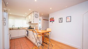 A compact kitchen with a wooden countertop, two foldable chairs, a sink, and a clock on the wall.