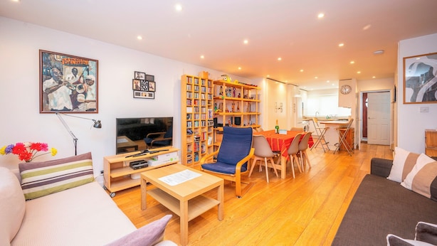 A living room with a sofa, a TV, a bookshelf, and a dining area with chairs and a table.