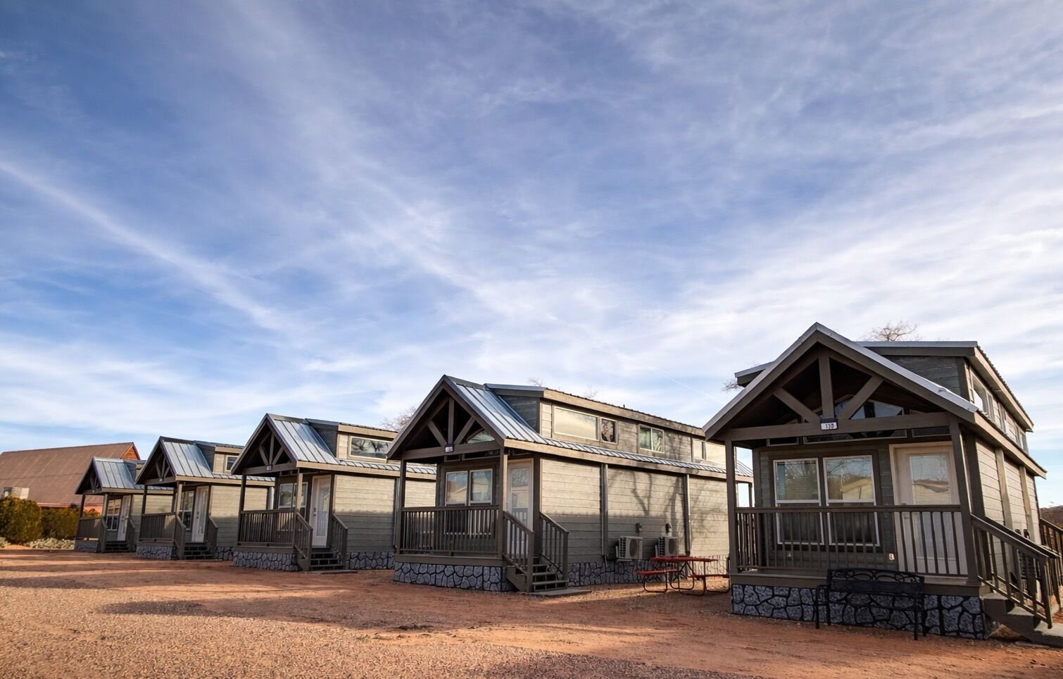 A row of modern cabins with sloped roofs and large windows, featuring stone foundations and wooden railings.