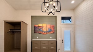 A bathroom with a wooden cabinet, a sink with a countertop, and a wall-mounted painting. - Luxury Tiny Homes - Deluxe King Room (Page)