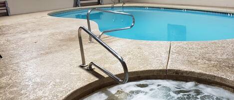 A swimming pool with a hot tub in the foreground, a bench, and a lifeguard chair.
