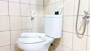 Des toilettes blanches avec une serviette posée sur la lunette, un porte-rouleau de papier toilette et un pommeau de douche à main.