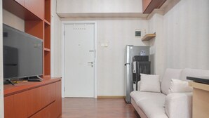 Ein kompakter Wohnbereich mit Holzschrank, Flachbildfernseher, weißem Sofa und Kühlschrank.