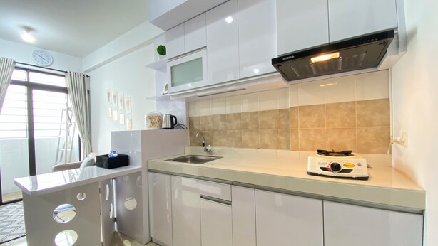 A modern kitchen with white cabinets, a stainless steel sink, a microwave, and a gas stove. - Homey 2Br Furnished Apartment At The Edge Bandung (Cimahi)