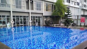 A swimming pool with a checkered pattern, surrounded by a building with large windows and a balcony. - Homey 2Br Furnished Apartment At The Edge Bandung (Cimahi)