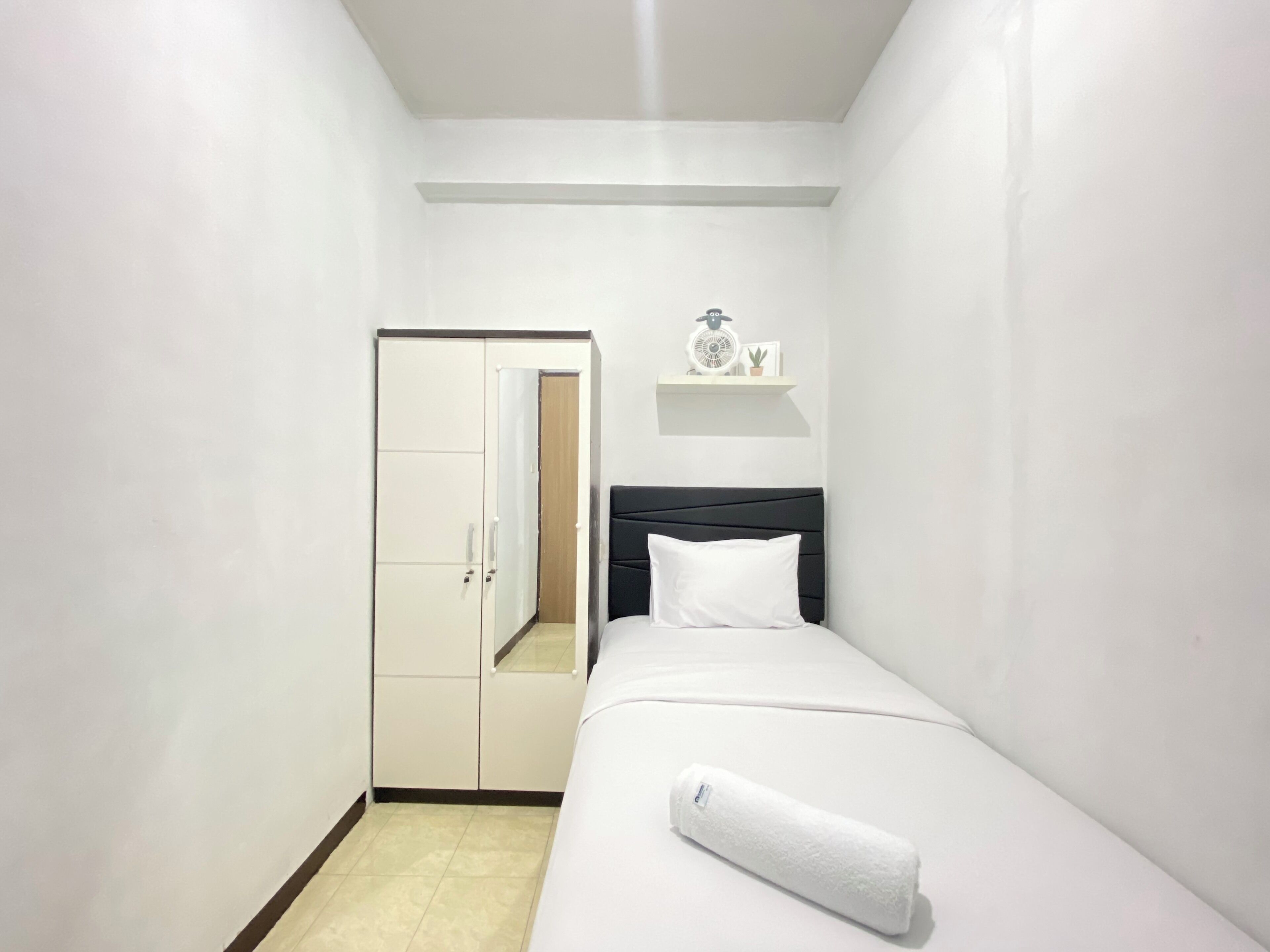 A small, neatly arranged bedroom with a bed, a bedside table, a shelf with a clock and a plant, and a wardrobe with a mirror.