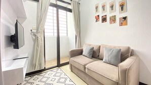 A modern living room with a beige sofa, a patterned rug, a mounted TV, and a window with curtains. - Homey 2Br Furnished Apartment At The Edge Bandung (Cimahi)