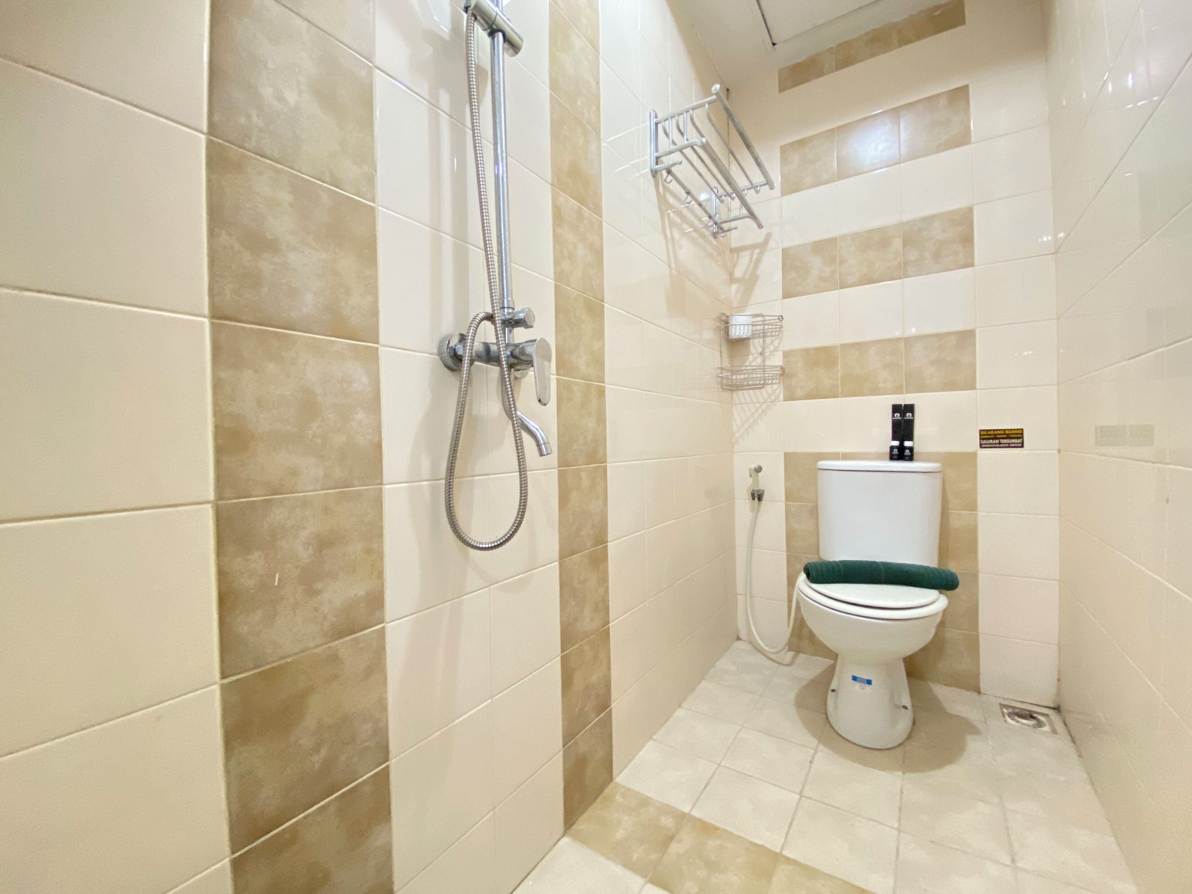 A bathroom with beige tiles, a shower, a toilet, and a towel rack.