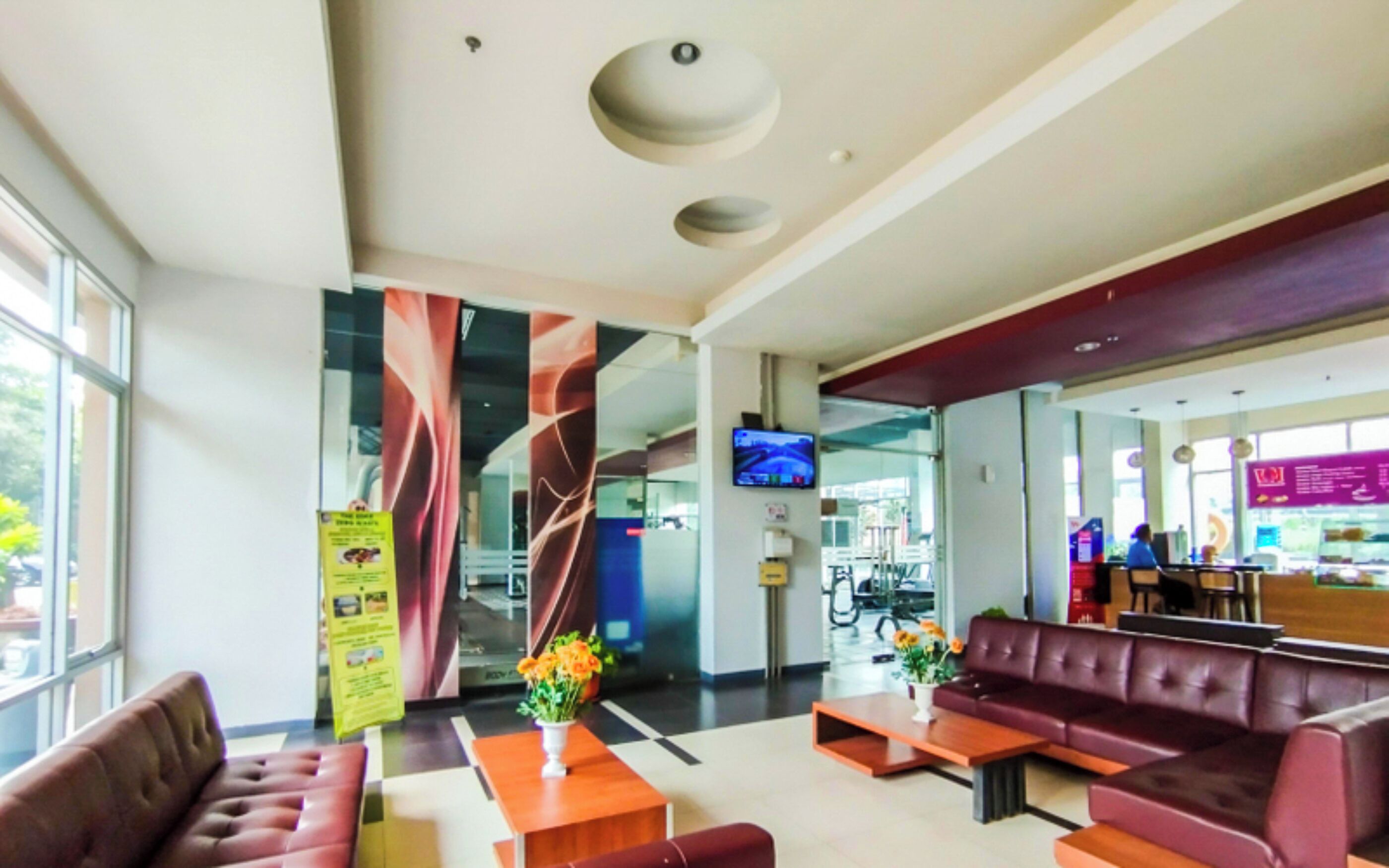 A modern lobby with seating areas, a TV screen, and a glass wall offering a view of the outside.
