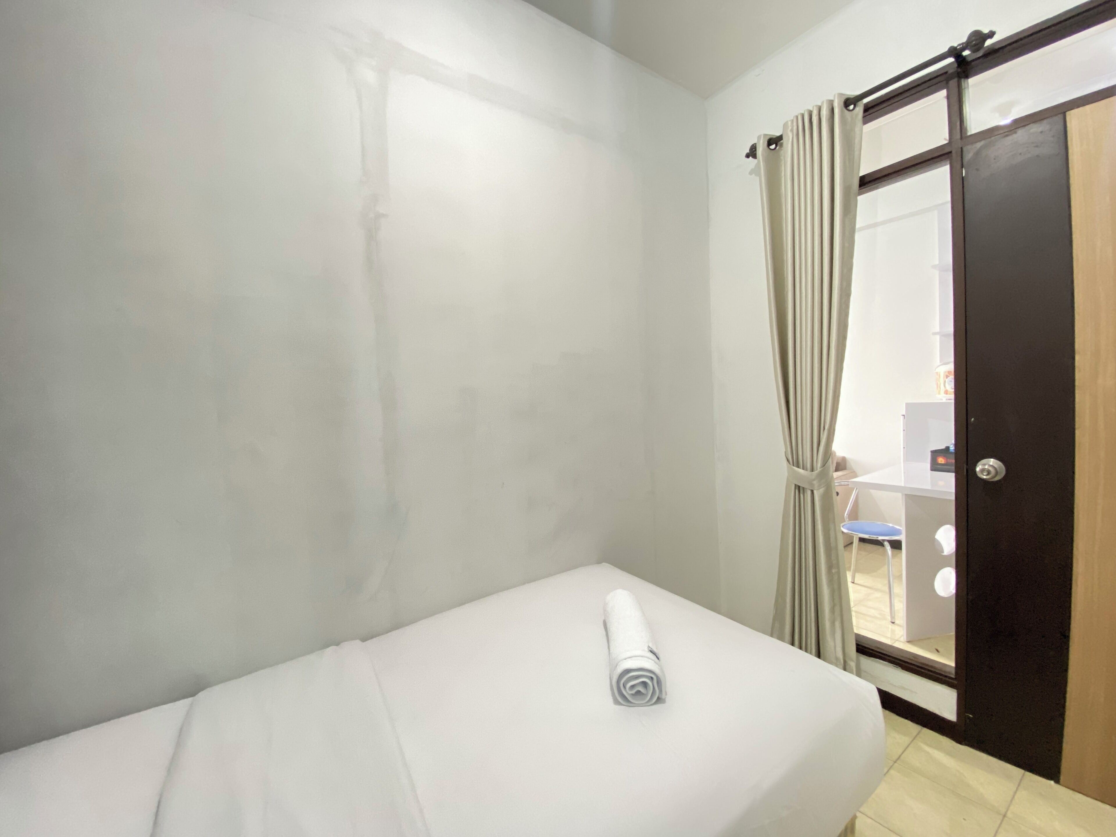 Een kleine, schone kamer met een enkel bed, een deur naar een badkamer en een gordijn.