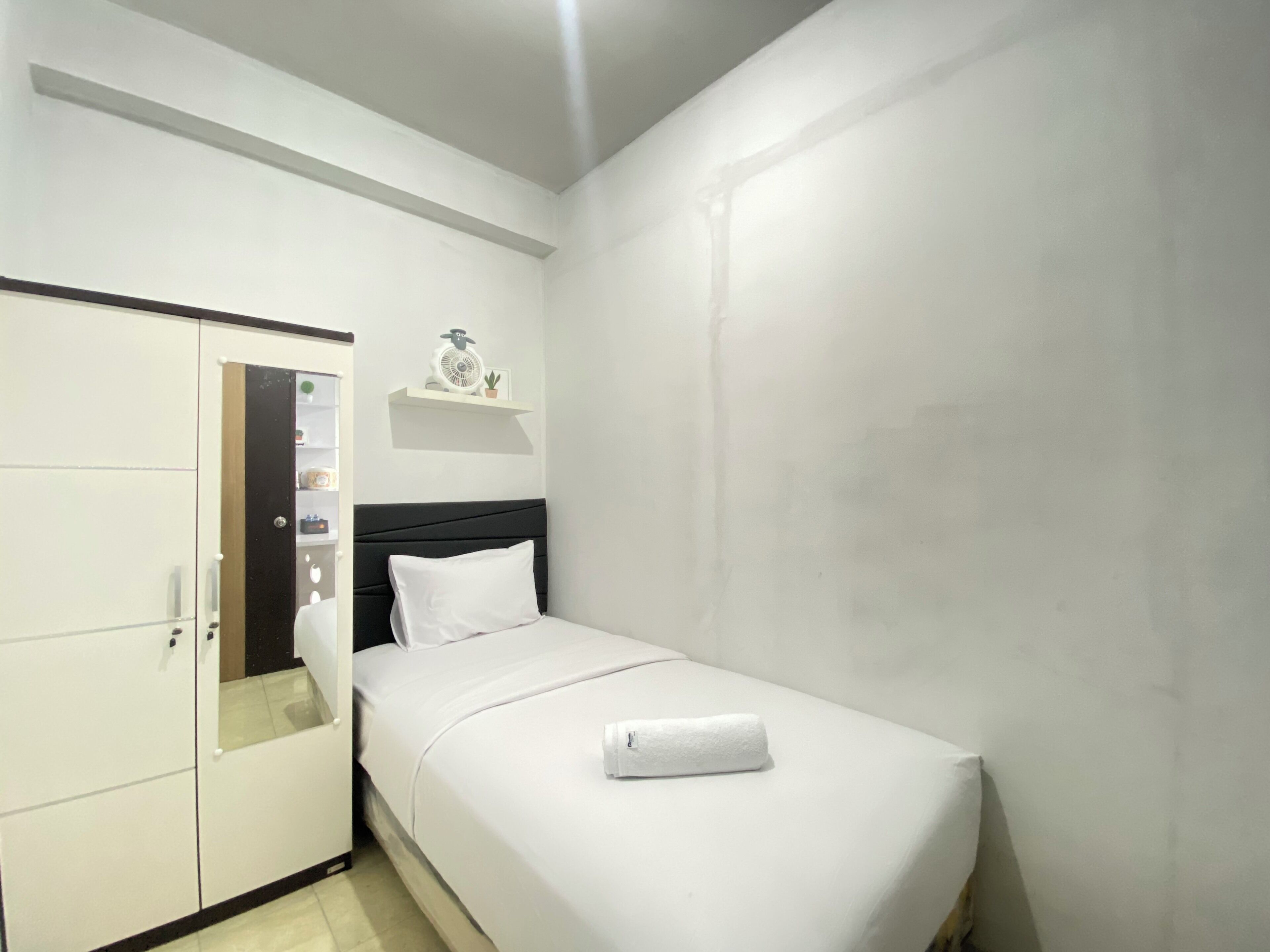 A small, neatly arranged bedroom with a single bed, a wardrobe, and a shelf with a clock and a plant.