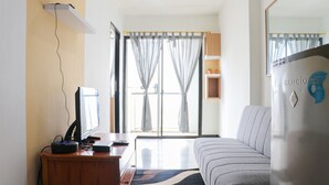 Una sala moderna con un sofá, un escritorio con una computadora y un amplio ventanal con cortinas.