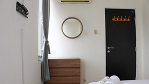 Un dormitorio con un aparador de madera, un espejo redondo, una puerta negra con perchero y una ventana con cortina.