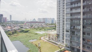 A high-rise building with multiple balconies, a grassy area with a small pond, and a distant view of a cityscape with various buildings. - Full Furnished And Homey Studio At Daan Mogot City Apartment (Jakarta)