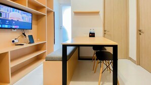 Et moderne værelse med fjernsyn på en hylde, et skrivebord med stol og en dør.