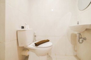 A small, clean bathroom with a toilet, a sink, and a towel on the toilet seat. - Simply And Homey Studio At Evenciio Margonda Apartment (Depok)
