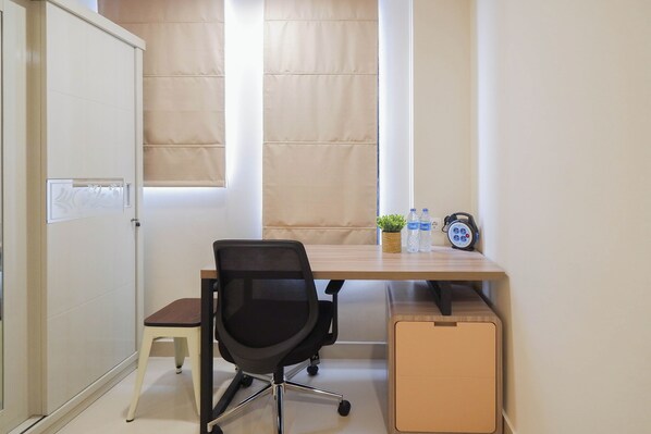 Un espacio de oficina pequeño con escritorio, silla, radiador, ventana y un taburete bajo.