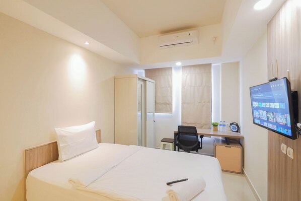A hotel room with a bed, a desk, a chair, a television, and an air conditioning unit. - Simply And Homey Studio At Evenciio Margonda Apartment (Depok)