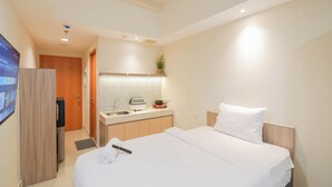 A hotel room with a bed, a small kitchenette, a TV, and a door leading to a bathroom.