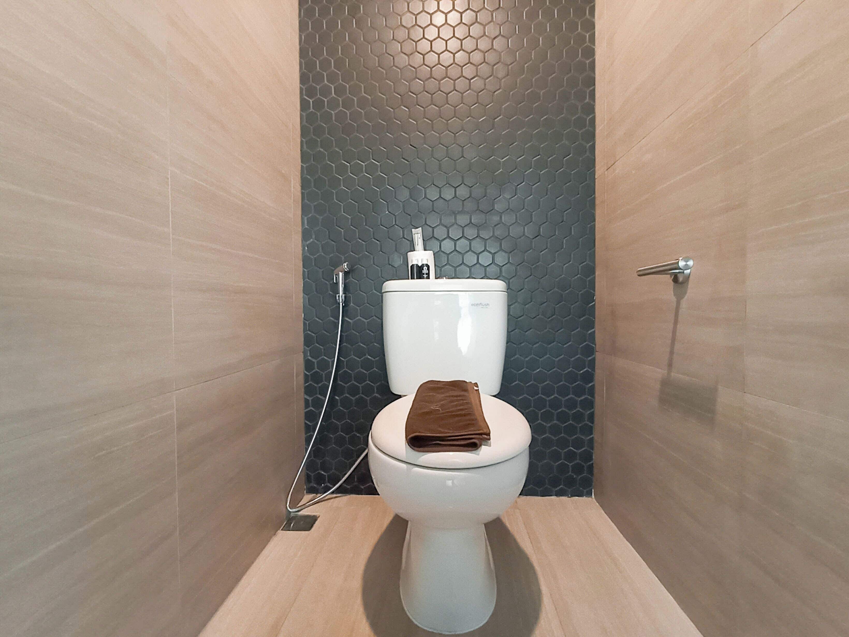 A modern bathroom with a hexagonal tile backsplash, a toilet, and a towel on the seat.