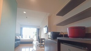 A modern hotel room with a bed, a desk, a red pot, and a GE appliance. - Comfort Studio (No Kitchen) Apartment At Skales Residence Nusa Dua Bali (Nusa Dua)