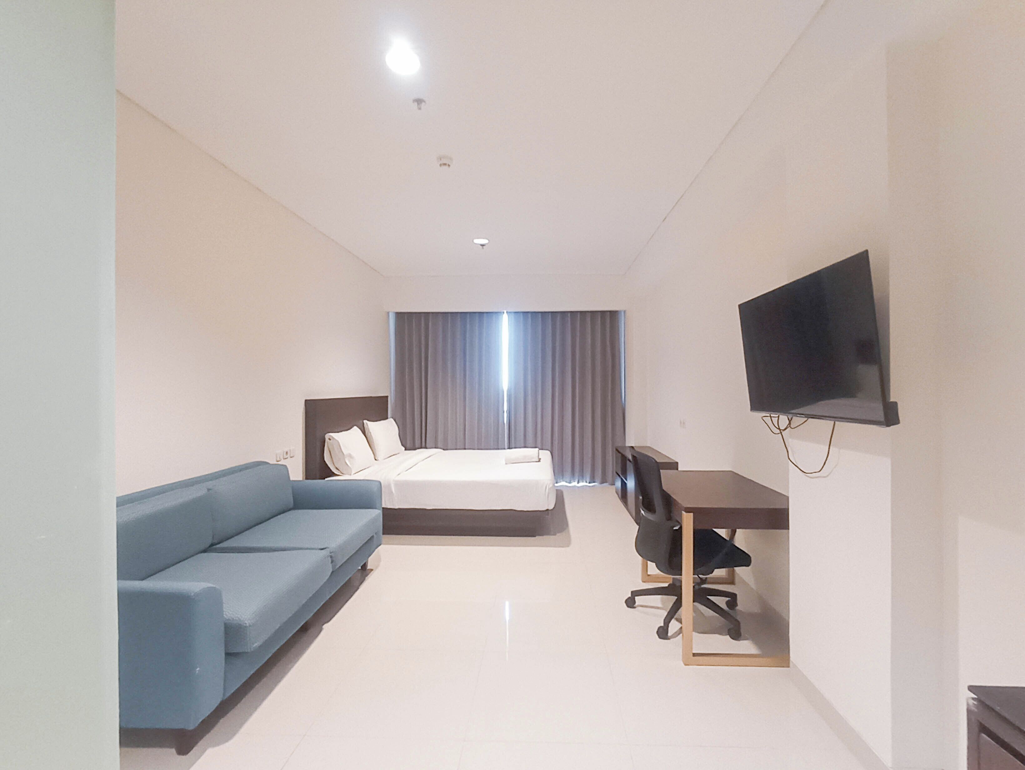 A hotel room with a bed, a blue sofa, a desk with a chair, and a TV mounted on the wall.