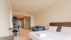 A hotel room with a bed, a desk, a chair, a sofa, and an air conditioning unit. - Comfort Studio (No Kitchen) Apartment At Skales Residence Nusa Dua Bali (Nusa Dua)