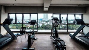 Un gimnasio con equipamiento de ejercicio y amplios ventanales que ofrecen vistas a la ciudad.