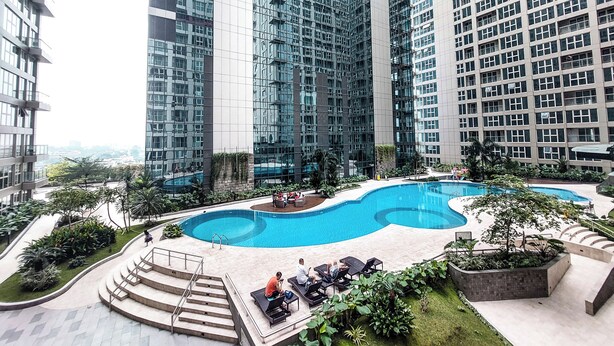 Un edificio moderno de gran altura con una piscina central rodeada de zonas de descanso y vegetación.