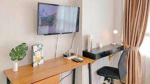 Une chambre d’hôtel équipée d’un téléviseur à écran plat fixé au mur, d’un bureau en bois avec une télécommande, d’un routeur et d’une boîte de parfum.