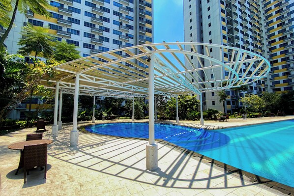 Una piscina con un porche blanco, rodeada de sillones de descanso y un solárium con baldosas.