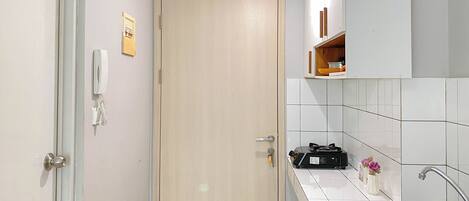 A kitchen with a wooden door, white tiles, a sink, and a small shelf with items.